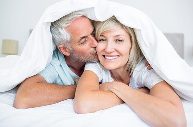 An adult couple lies under a blanket