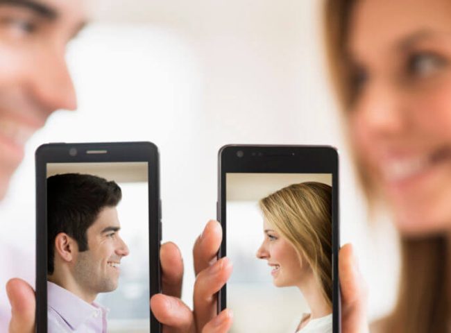 A woman and a man taking pictures of themselves on different phones